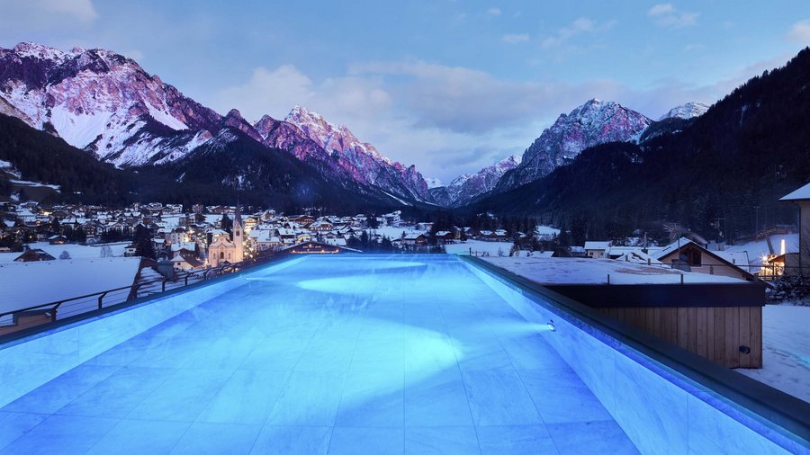 South Tyrol: wellness holiday à la Excelsior Lit outdoor pool with snowy village and mountains in the background