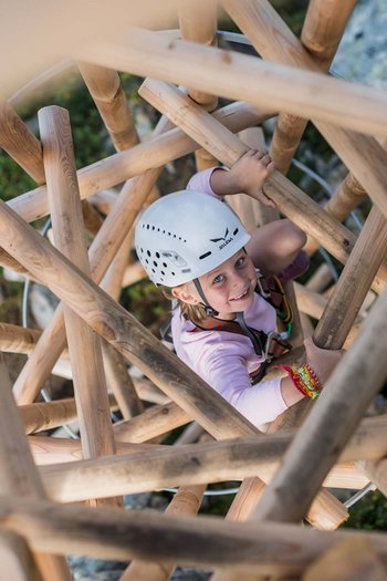 Family-friendly hotel in South Tyrol Child climbing a wooden structure outdoors wearing a helmet