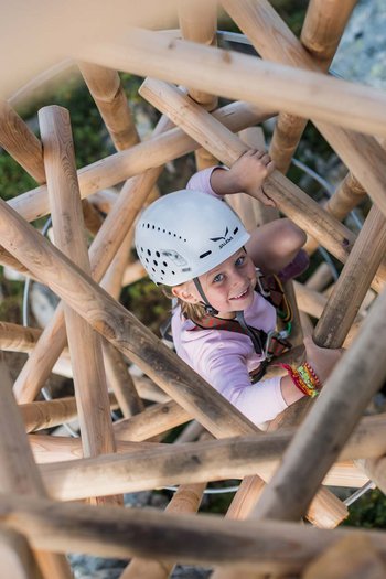 Familienurlaub in den Dolomiten – Natur, Erholung & Abenteuer Kind klettert mit Helm auf Holzstruktur im Freien
