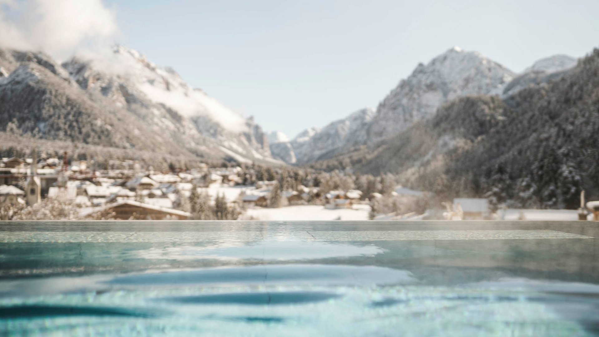 Wellnesshotel in den Dolomiten Infinity-Pool mit Blick auf schneebedeckte Berge und ein Dorf