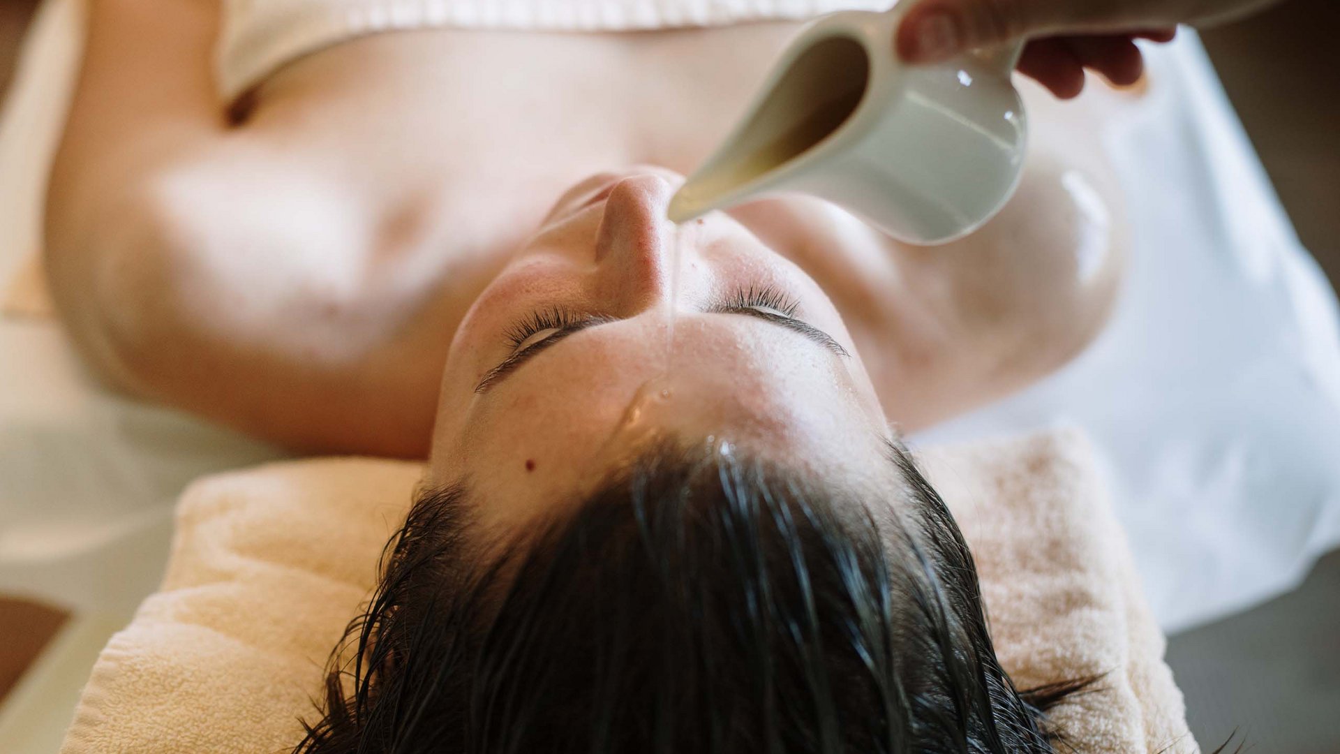 Massagen im Wellnesshotel am Kronplatz Frau bei Spa-Behandlung, Gesicht wird mit Wasser vom Krug benetzt