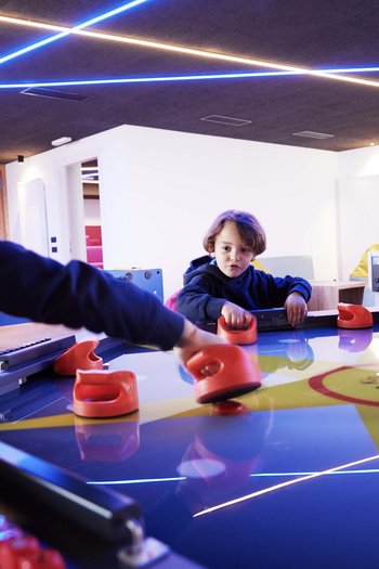Excelsior: hotel wellness in Alto Adige per famiglie Tre bambini giocano a air hockey a un tavolo illuminato all'interno