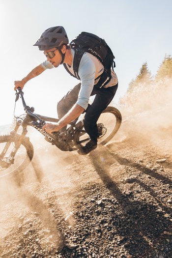 Excelsior: Wanderhotel in den Dolomiten Mountainbiker fährt staubigen steilen Weg im Sonnenlicht hinunter
