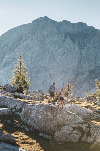 Excelsior: Wanderhotel in den Dolomiten Zwei Wanderer auf felsigem Bergpfad mit sonnigem Hintergrund