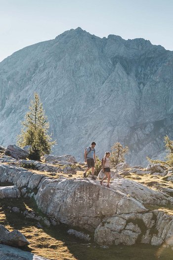 Wanderhotels Südtirol in the Dolomites Two hikers on rocky mountain trail with sunlight in background