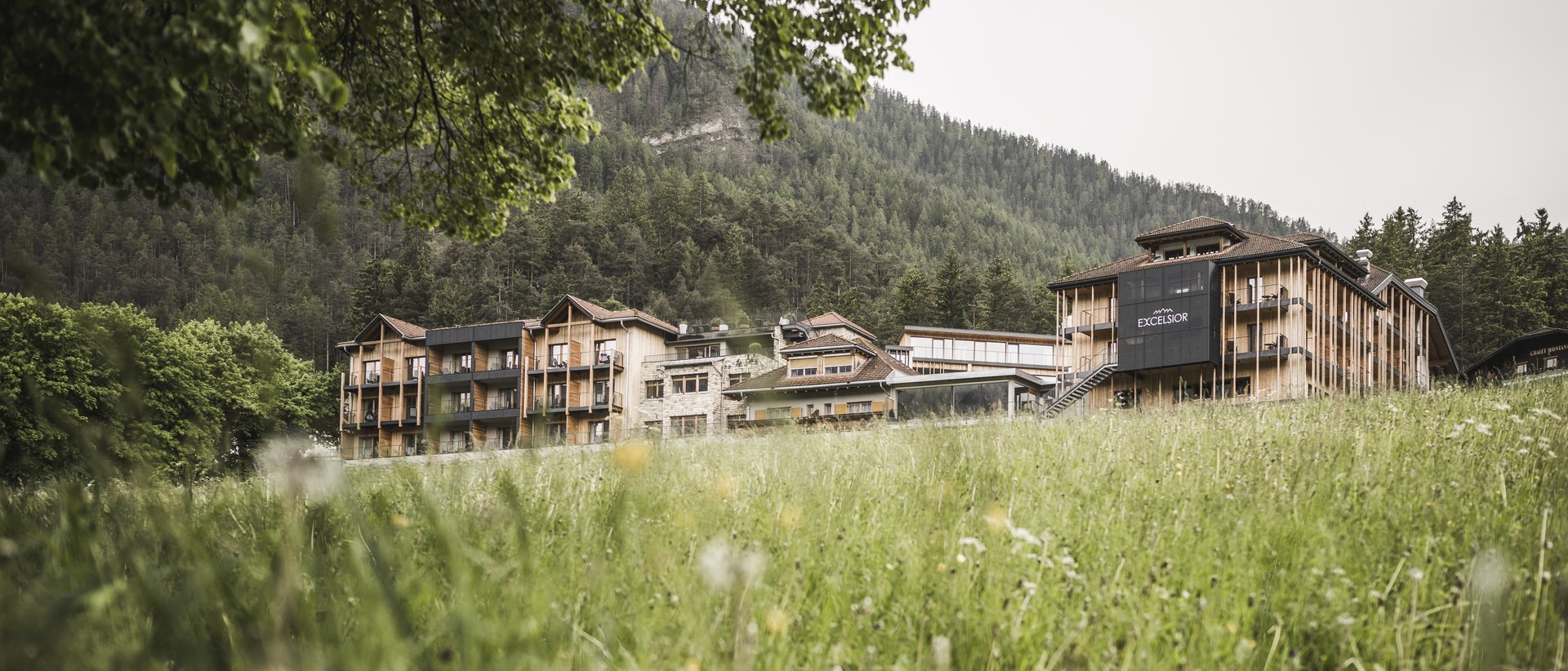 Neue Aussenfassade Hotel Excelsior umgeben von Wiese und Bergen im Hintergrund