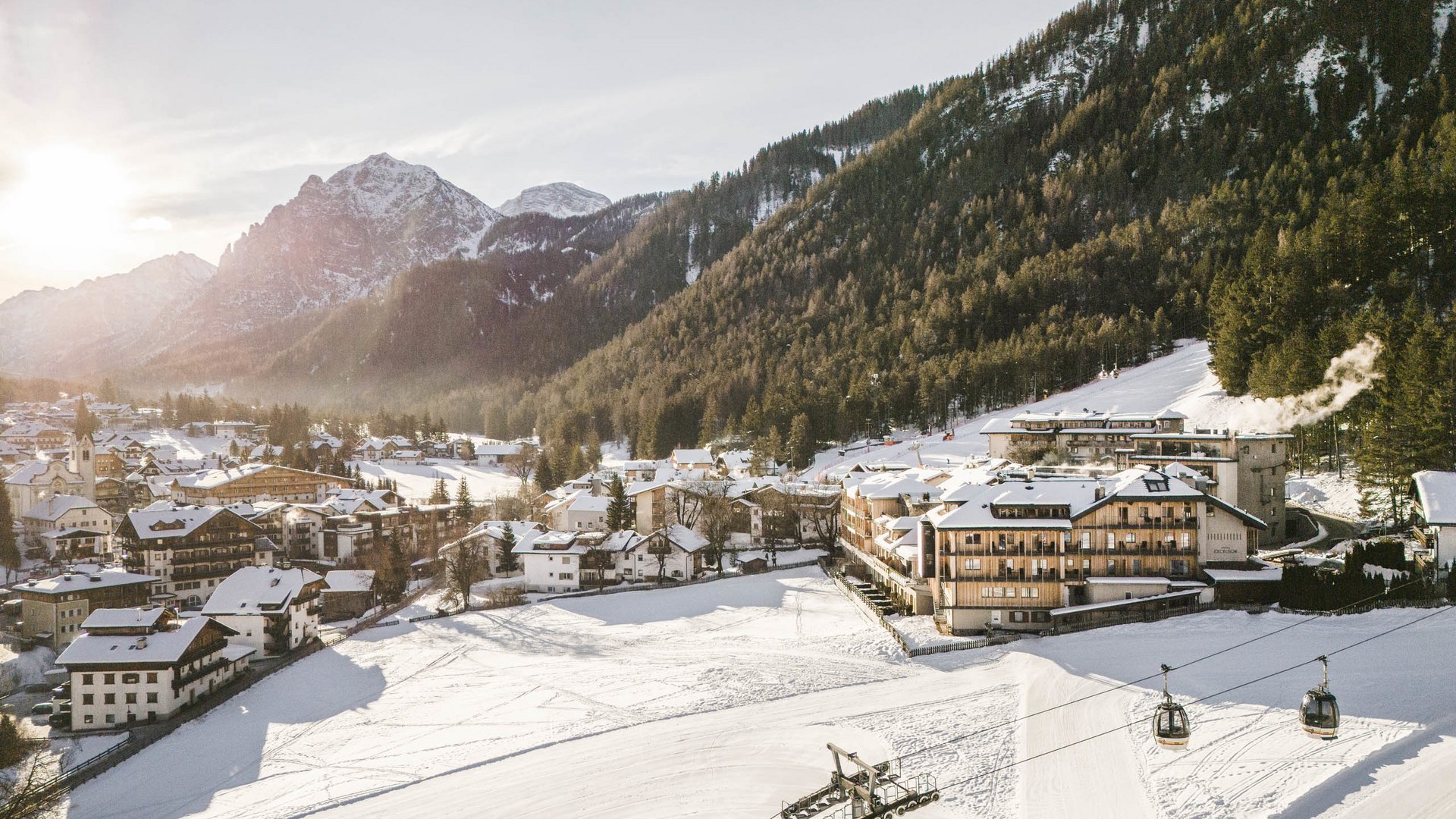 Winterwandern in den Dolomiten rund um das Excelsior Schneebedecktes Bergdorf mit Seilbahnkabinen und sonnigem Himmel
