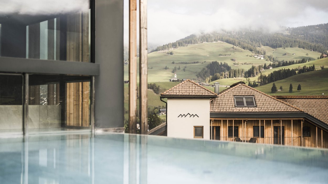 Sustainable hotels in South Tyrol? The Excelsior! Infinity pool overlooking a house and green hills in the mountains