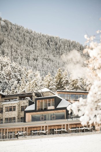 Wellnesshotel in Südtirol: Auf in den Traumurlaub! Modernes Hotel vor einem verschneiten Waldhang im Winter