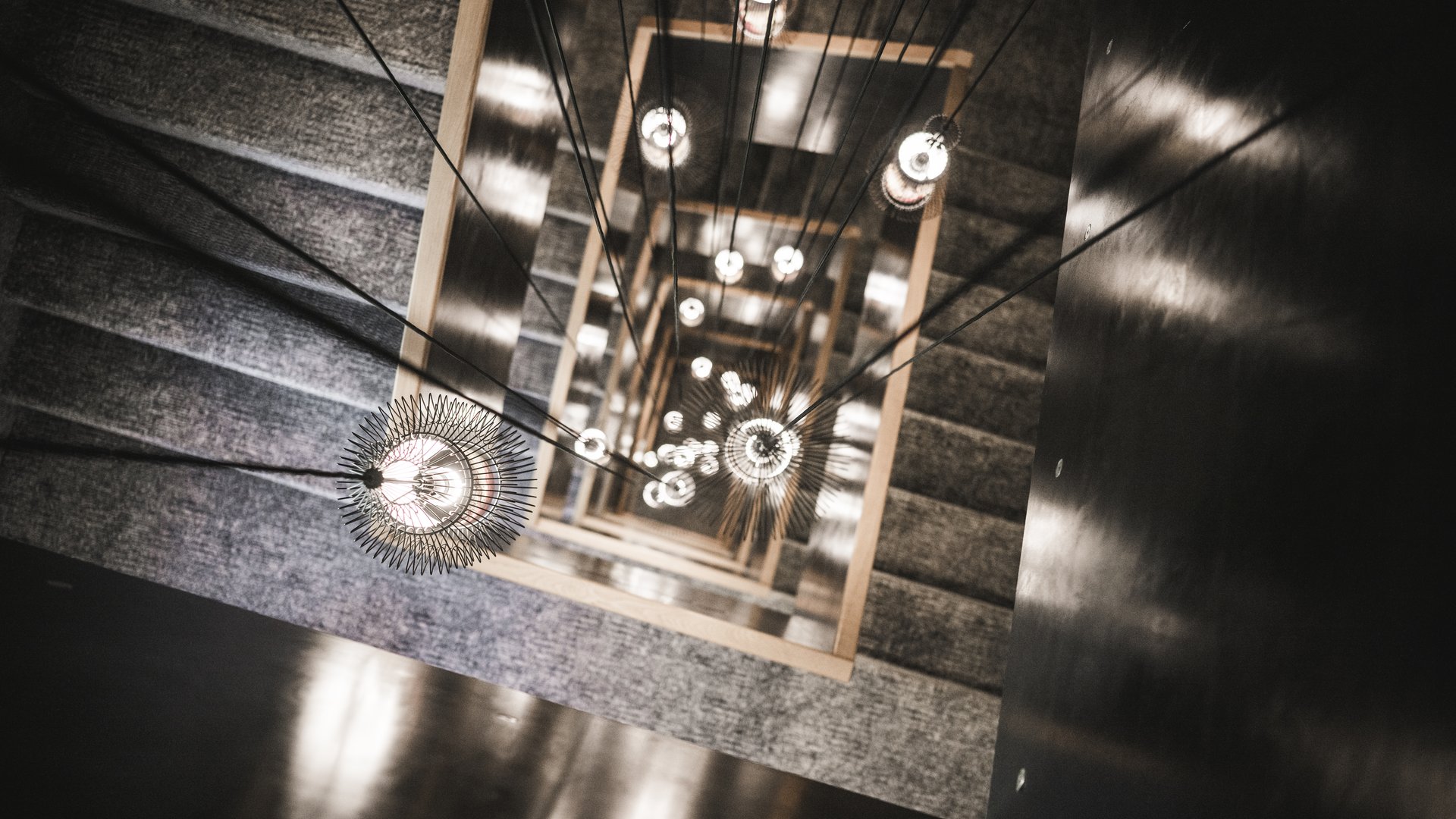 Kunst im Designhotel in Südtirol Blick von oben auf eine quadratische Treppe mit hängenden Lampen