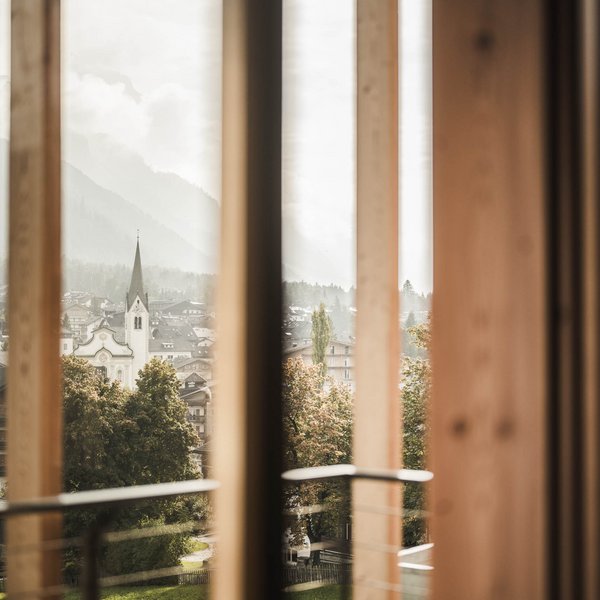 Wellnesshotel in Südtirol: Auf in den Traumurlaub! Blick durch ein Fenster auf ein Dorf mit Kirchturm und Berge