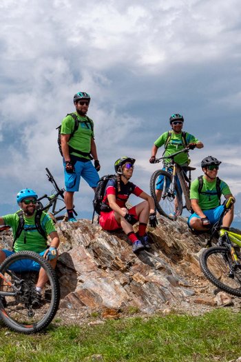 Bike offers and impressions Six mountain bikers resting on a rock with bikes in mountainous area