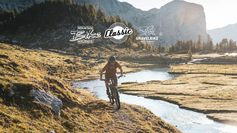 Bike-Kompetenz Mountainbiker fährt an Fluss in bergiger Landschaft mit Sonnenlicht