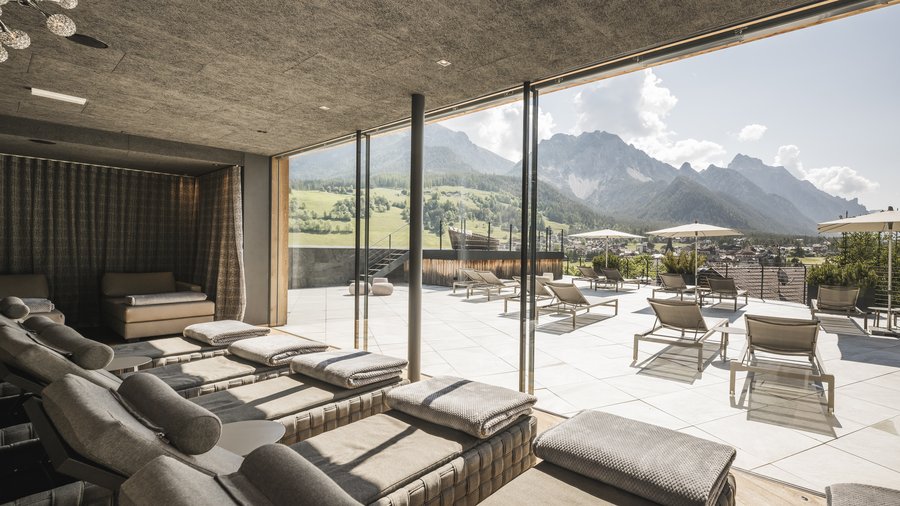 Kurzurlaub in Südtirol? Im Excelsior Dolomites Life Resort Entspannungsbereich mit Liegestühlen und Blick auf Berge bei Sonnenlicht