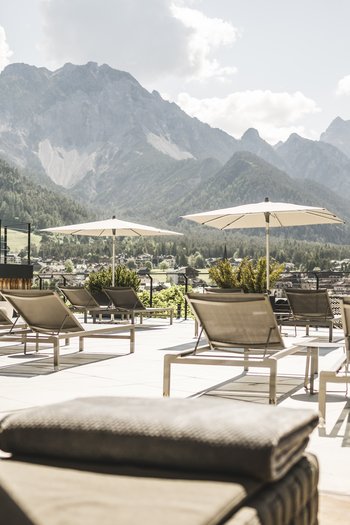 Hotel con infinity pool in Alto Adige: l’Excelsior Terrazza soleggiata con lettini e vista sulle montagne sullo sfondo