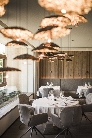 Molto più di un hotel a San Vigilio di Marebbe! Ristorante elegante con tavoli rotondi apparecchiati e luci calde sospese