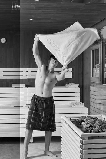 Ihr Hotel in St. Vigil in Enneberg! Mann fächert mit Handtuch in einer modernen Sauna mit Holzverkleidung und Steinen.