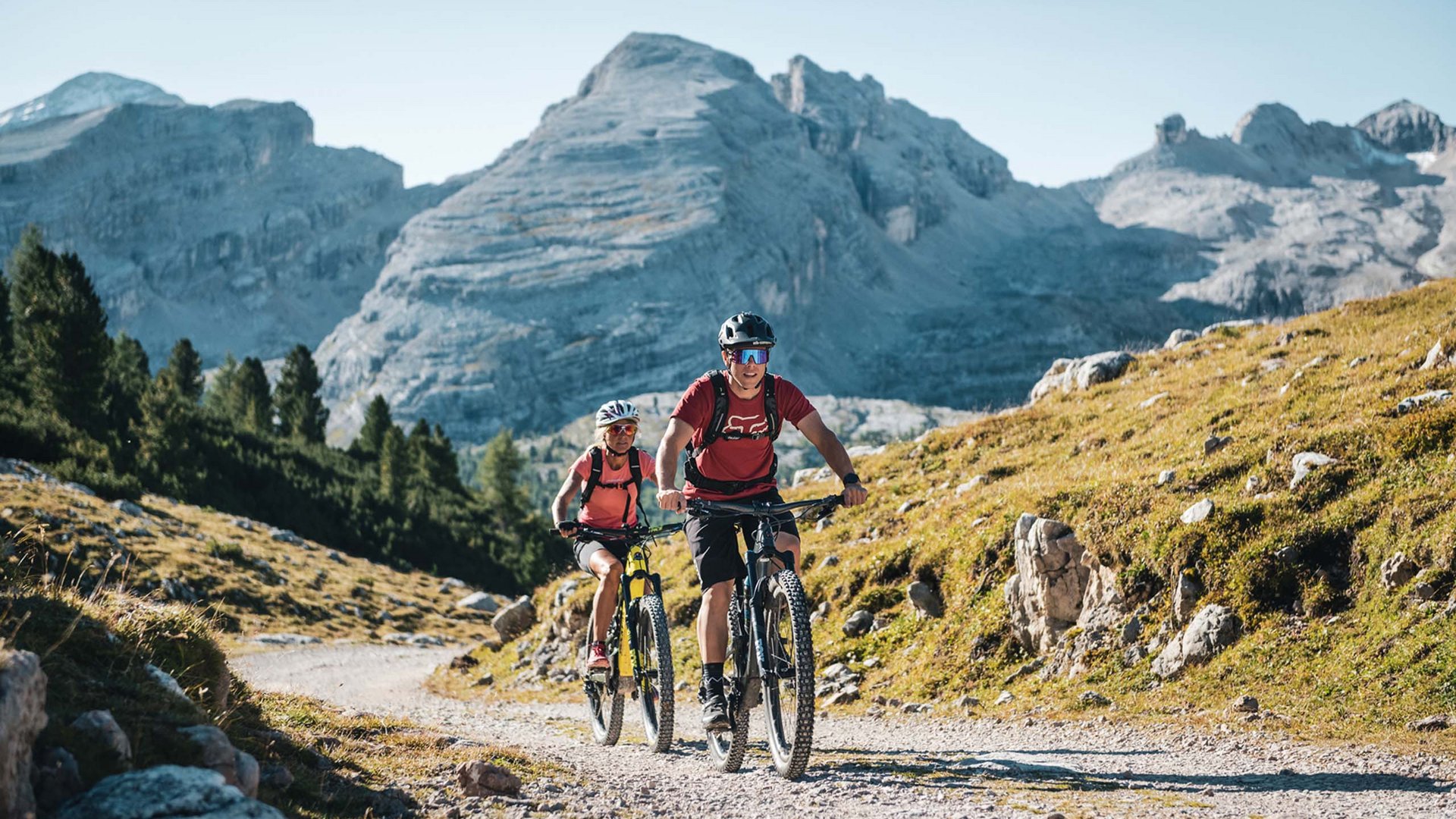 Wandern und Wellness: Ihr Aktivhotel in Südtirol Zwei Mountainbiker fahren auf Bergweg mit Felsen und Bäumen im Hintergrund
