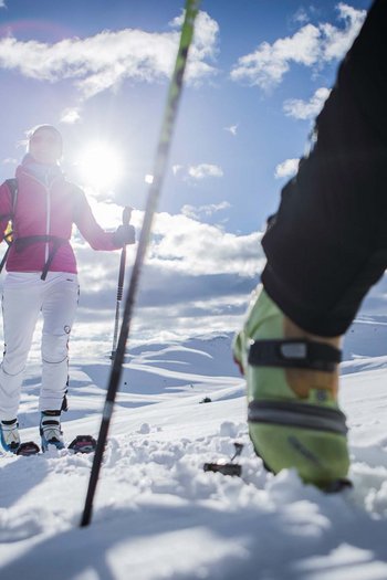 Hotel at Plan de Corones/Kronplatz on the slopes Two people snowshoeing in sunny snowy mountain landscape