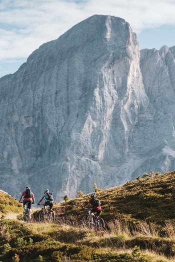 Eines der Bike-Hotels in Südtirol Drei Radfahrer fahren auf einem Bergpfad mit großem Felsen im Hintergrund