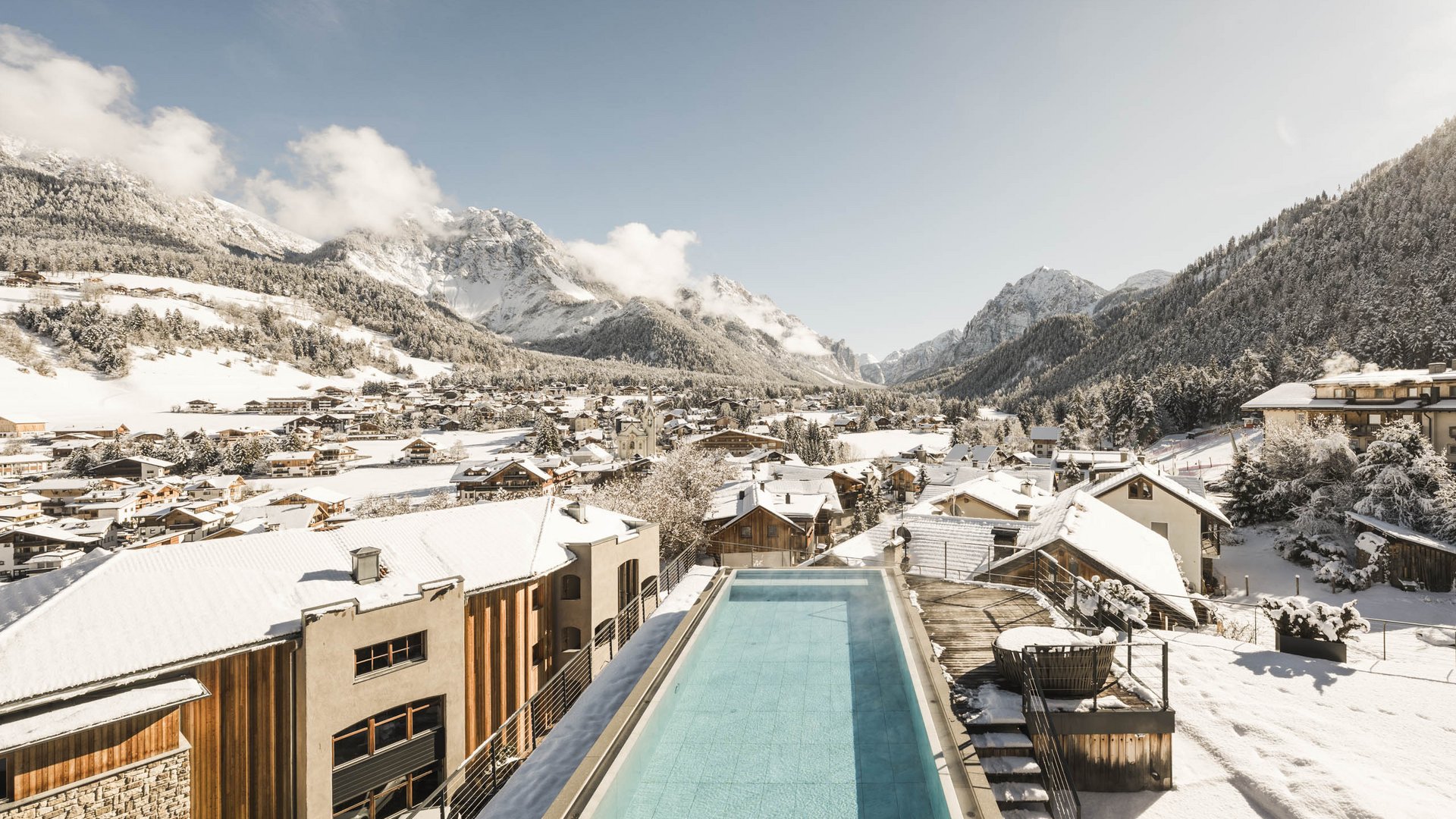 Wellnesshotel in den Dolomiten Beheizter Pool auf Dach mit Blick auf schneebedeckte Alpen und Dorf