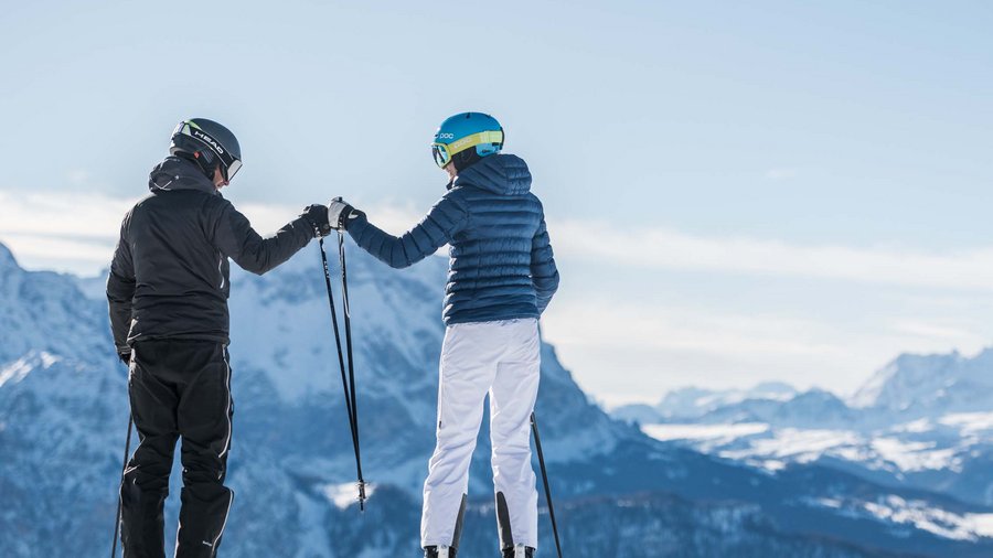 Plan de Corones, in Alto Adige: attività e highlight Due sciatori si danno il cinque davanti a montagne innevate