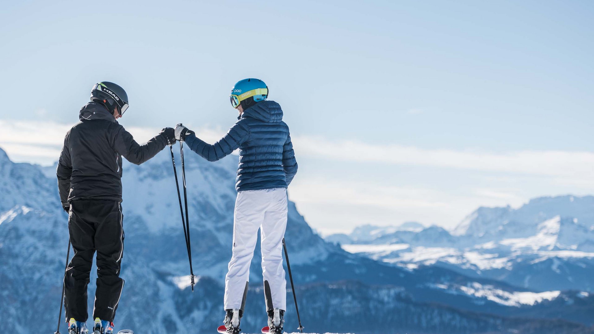 Events: Excelsior Dolomites Life Resort Two skiers fist bump with snowy mountains in the background