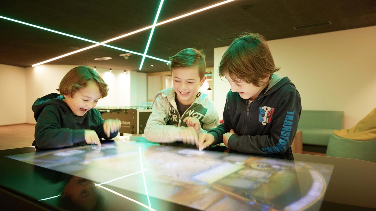 Family-friendly hotel in South Tyrol Three kids happily playing on an interactive touchscreen table