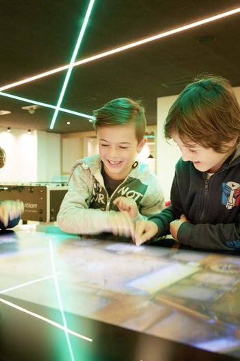 Family-friendly hotel in South Tyrol Three kids happily playing on an interactive touchscreen table