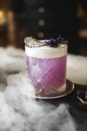 Das Gourmethotel in Südtirol Lila Cocktail mit Schaum und Früchten auf einem Tablett mit Nebel