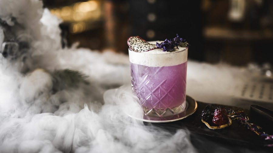 Luxushotel in den Dolomiten | Excelsior in St. Vigil Lila Cocktail mit Schaum und Früchten auf einem Tablett mit Nebel