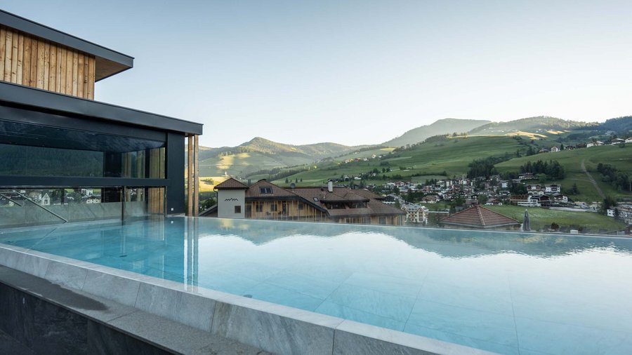 Excelsior: membro dei Belvita Leading Wellnesshotels Südtirol Piscina a sfioro con vista su colline e case in una valle soleggiata