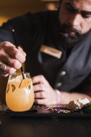 Wellnesshotel in Südtirol: Auf in den Traumurlaub! Barkeeper dekoriert einen Cocktail mit Pinsel und Blattgold