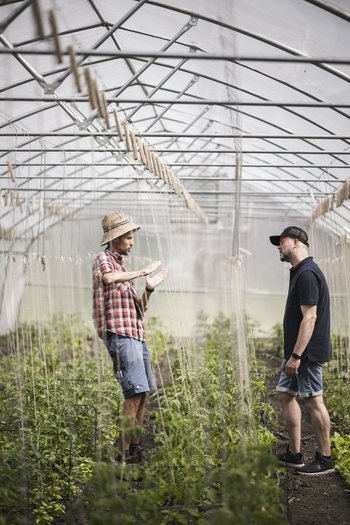 The gourmet hotel in South Tyrol Two men talking in a greenhouse surrounded by plants.