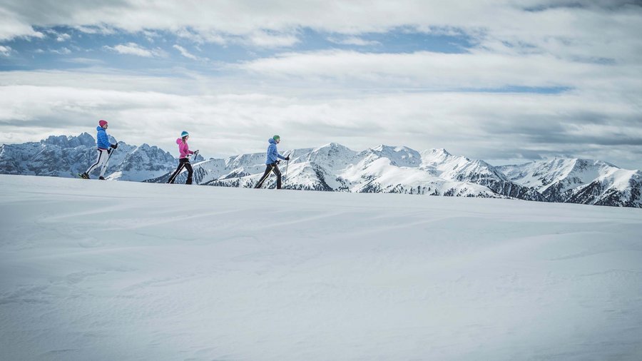Winterwandern in den Dolomiten rund um das Excelsior Drei Personen beim Skilanglauf auf schneebedecktem Bergplateau mit Bergblick