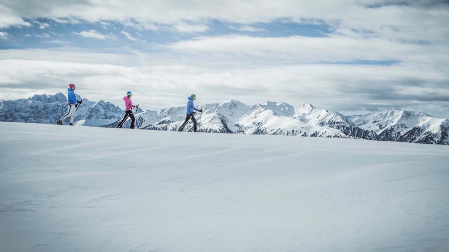 Winterwandern in den Dolomiten rund um das Excelsior Drei Personen beim Skilanglauf auf schneebedecktem Bergplateau mit Bergblick