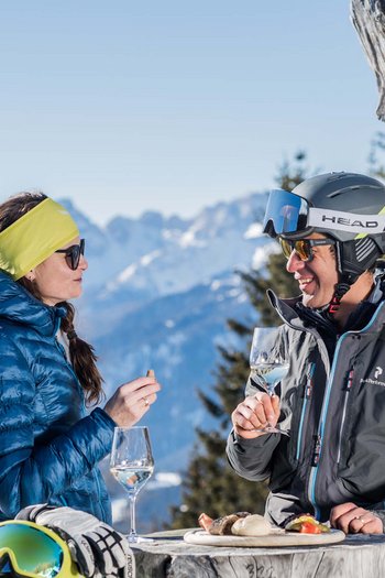 Hotel am Kronplatz direkt an der Piste Zwei Skifahrer genießen Wein und Brot an einem Tisch in den Bergen