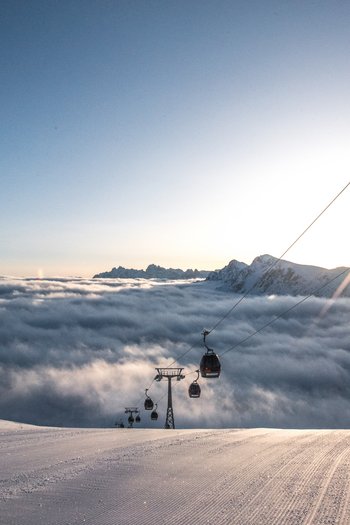 Around the hotel on the slopes in South Tyrol Ski lift over snowy slope at sunrise above sea of clouds and mountains