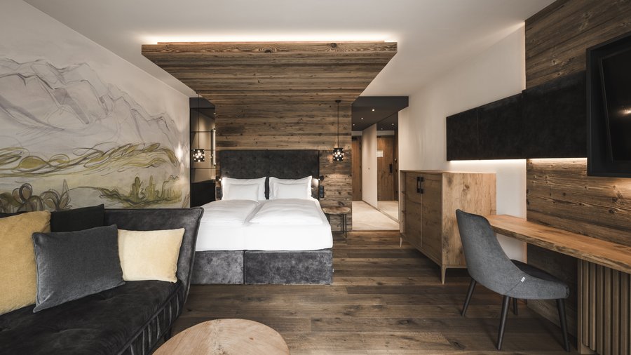 Art in the design hotel in South Tyrol Modern hotel room with double bed, sofa, and wooden furniture
