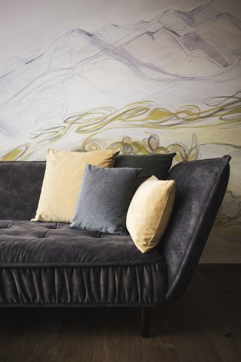 Art in the design hotel in South Tyrol Dark sofa with four colorful cushions in front of an abstract wall mural