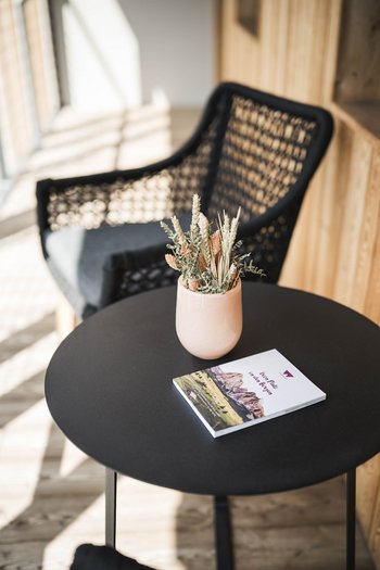 More than a hotel: Excelsior Black round table with dried flowers and brochure, black chair in background