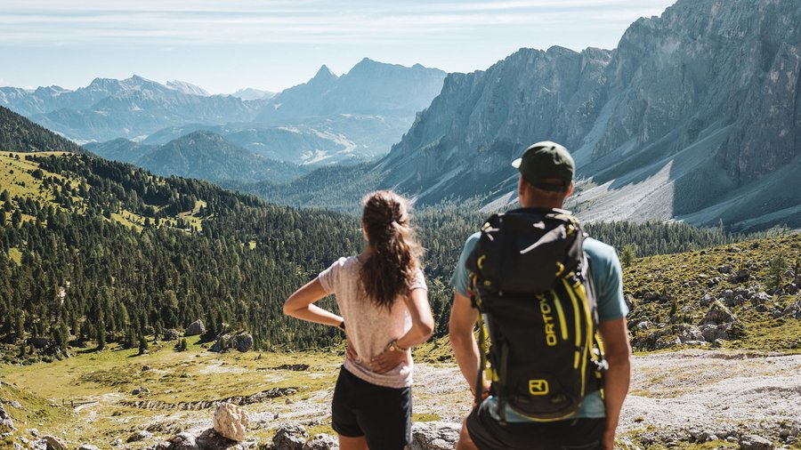 kurzurlaub-suedtirol Zwei Wanderer blicken auf bewaldete Berge und Felsklippen