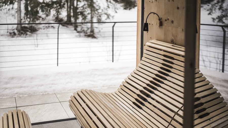 Wellnesshotel in den Dolomiten Holzbank vor Winterlandschaft mit Schnee und Bäumen