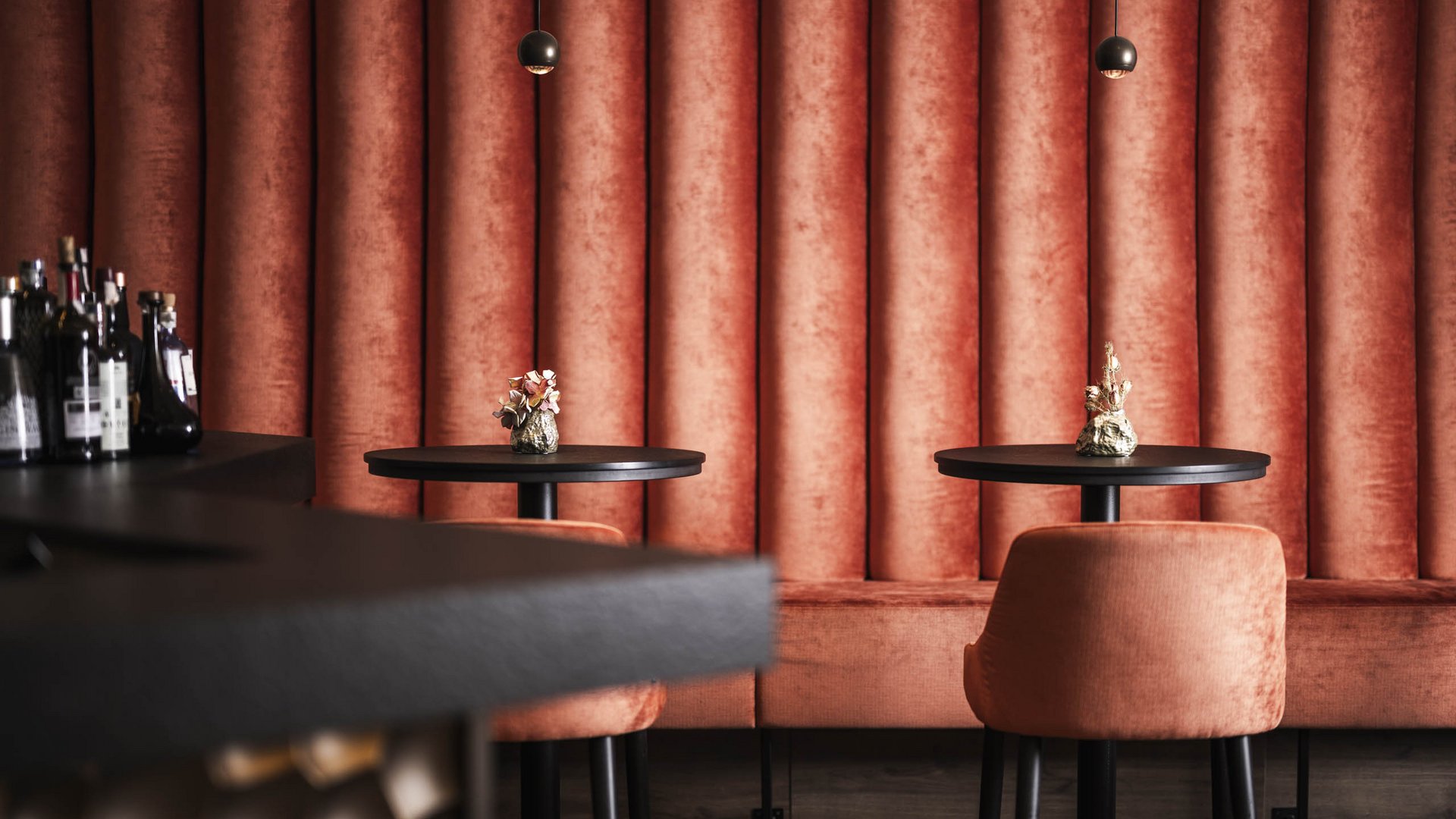 Ihr Hotel in St. Vigil in Enneberg! Moderne Bar mit orangen Samtstühlen und Tischen vor rotem Wandpaneel