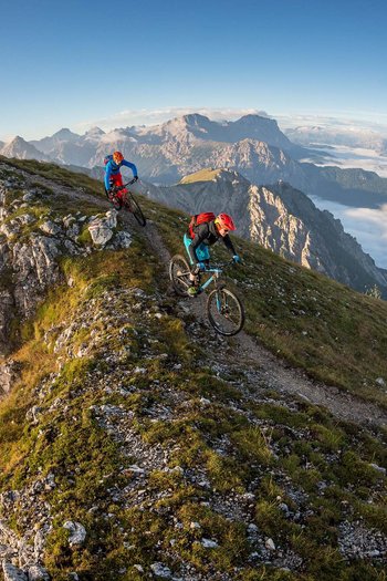 Il vostro sport hotel a San Vigilio di Marebbe Due ciclisti su un sentiero di montagna stretto con croce e nuvole sottostanti