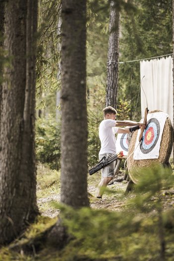 Family-friendly hotel in South Tyrol Man pulling arrow from archery target in forest