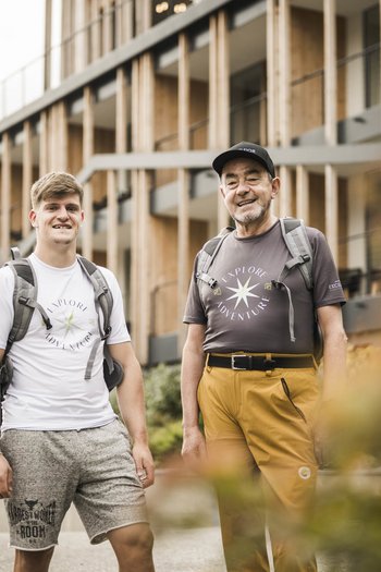 San Vigilio di Marebbe: escursioni per famiglie Due uomini con zaini davanti a edificio moderno all'aperto
