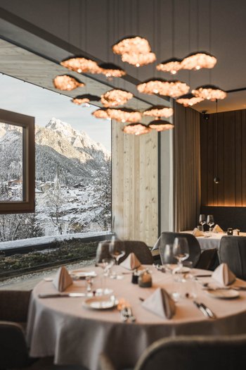 Wellnesshotel in Südtirol: Auf in den Traumurlaub! Elegantes Restaurant mit gedeckten Tischen und Blick auf ein verschneites Bergdorf