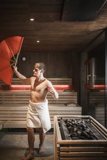Hotel con infinity pool in Alto Adige: l’Excelsior Uomo con asciugamano bianco che tiene un grande ventaglio rosso nella sauna