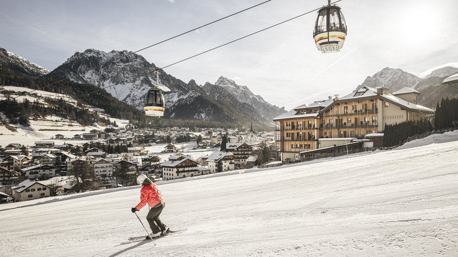 Wellness hotel in the Dolomites Skier on slope with cable cars and snowy mountain village background